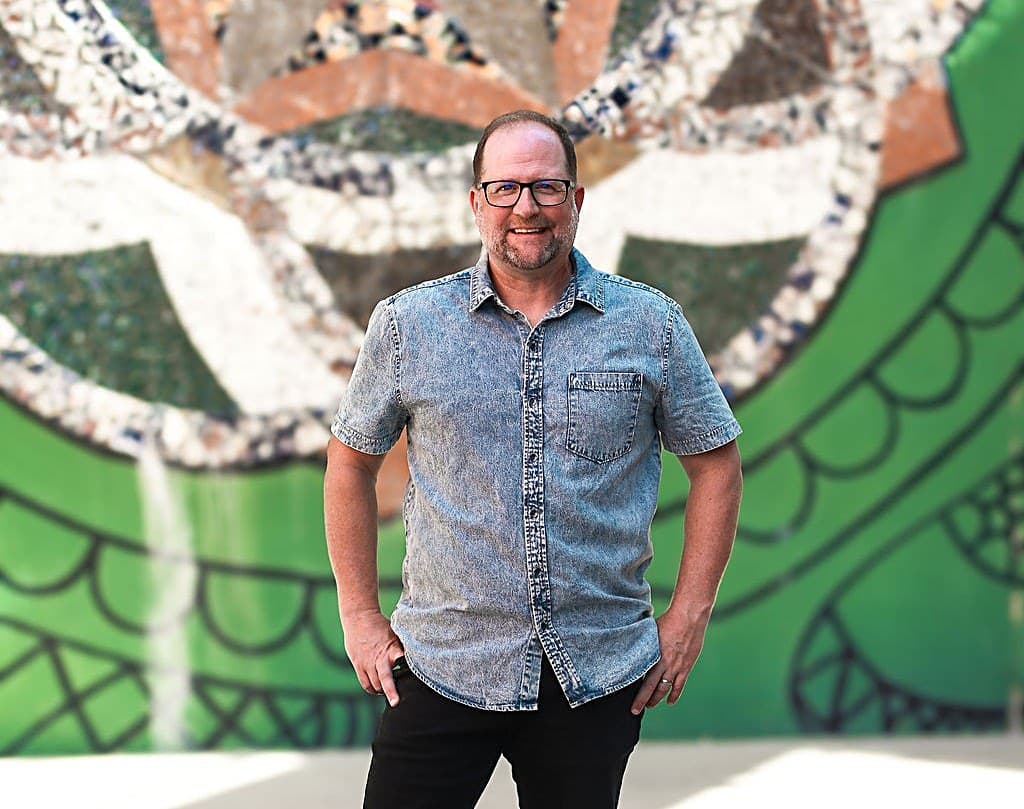 Jason Rolf, founder of IGOTCHU, standing in front of a mosaic mural